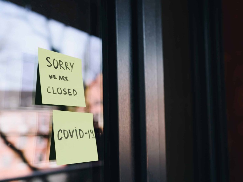 A photo of two Post-it notes stuck on a business's door that read (top to bottom) "Sorry We Are Closed" and "COVID-19".