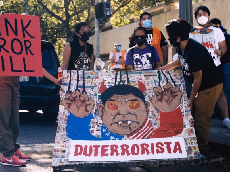 Filipino protesters hold up signs that read (left to right) Junk Terror Bill and Duterrorista. The latter poster has art of Rodrigo Duterte with devil horns.