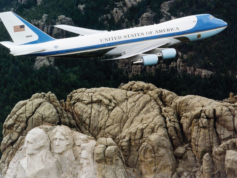 An image of a plane with United States of America written over it flying over Mount Rushmore.