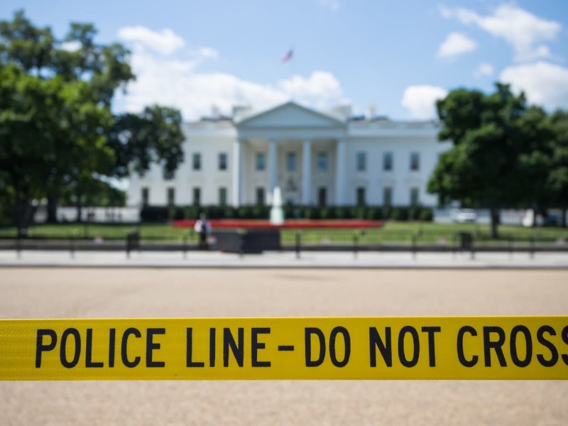 A photo of caution tape that says Police Line - Do Not Cross in front of the White House.