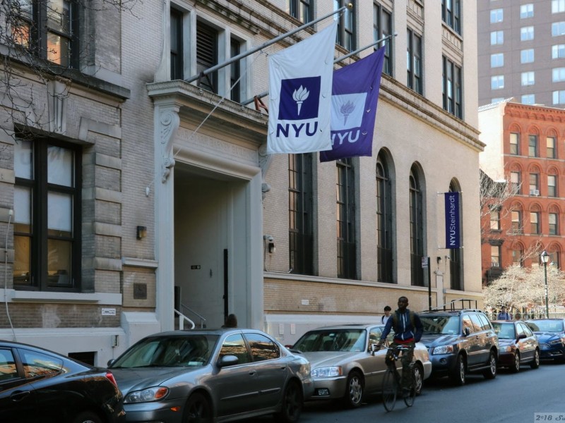 Two NYU flags fly outside a building of New York University.