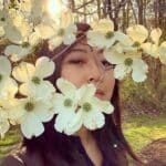 Photo of the author behind a branch of white flowers.