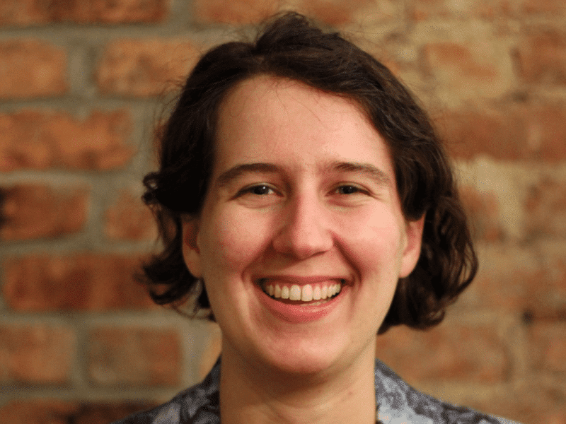 A headshot of Betsy Ladyzhets. She stands in front of a brick wall.