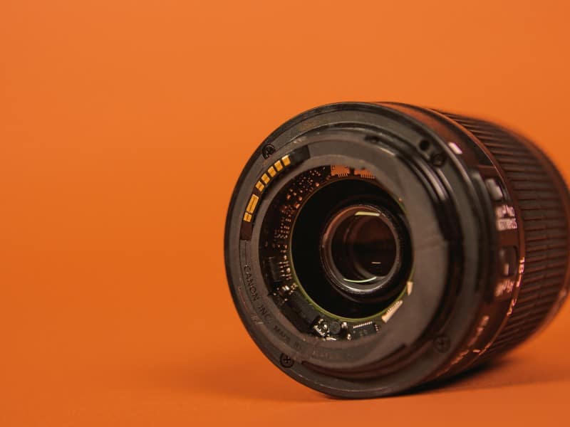 A broken camera lens on an orange backdrop.