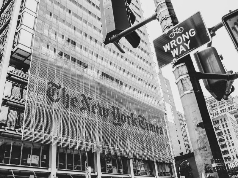 A photo of the New York Times' office building in New York. The image is black and white and a Wrong Way sign is in the foreground.