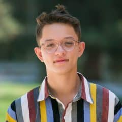 Headshot of Brandon Pho. He wears a striped button up shirt and is standing outside.