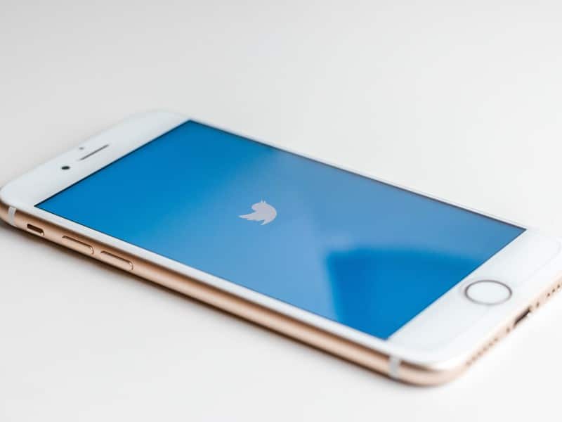 Photo of an iPhone laying on a flat surface. The Twitter logo is on the screen.