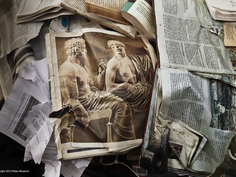 Crumpled newspapers lay on top of each other. The top newspaper has an image of two sculptures engaged in debate