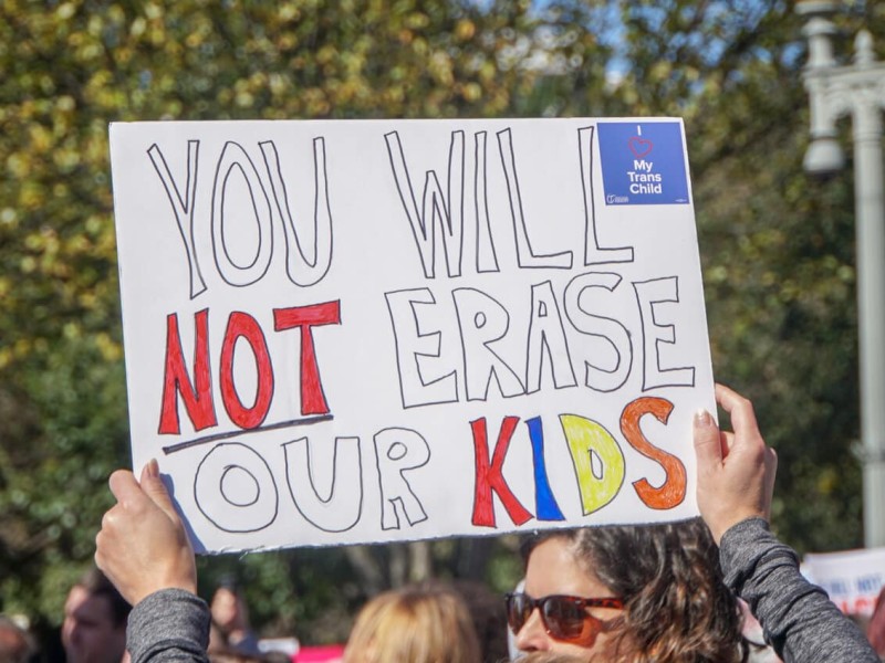 A protester marching for trans rights holds up a poster that reads You Will Not Erase Our Kids.
