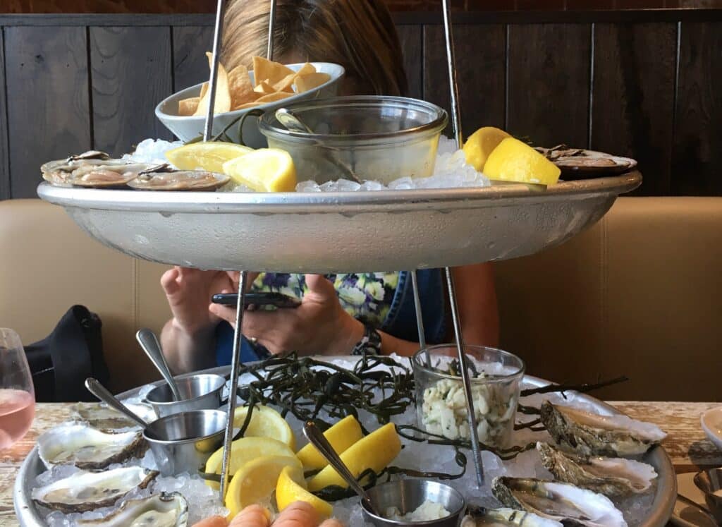 A tiered platter of seafood on ice, accompanied by lemons and chips, obscures Hanna Raskin, the author.