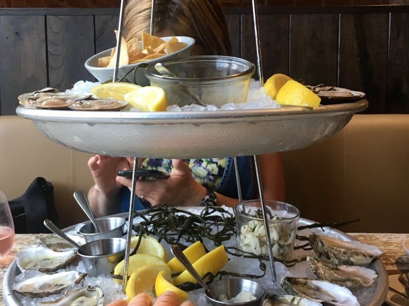 A tiered platter of seafood on ice, accompanied by lemons and chips, obscures Hanna Raskin, the author.