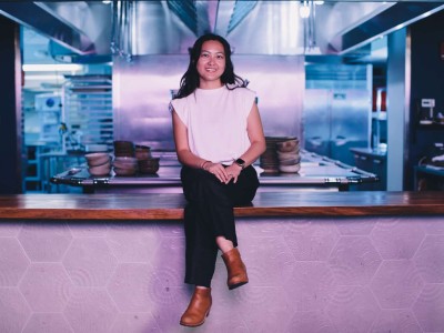 Jenny Dorsey, an Asian woman, sits cross-legged on the counter of an empty kitchen and smiles.