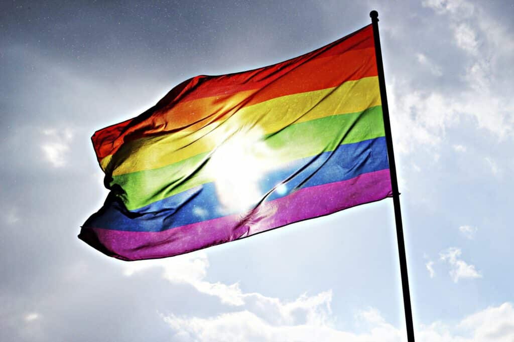 A photo of the pride flag against a pale blue sky, covering the sun.