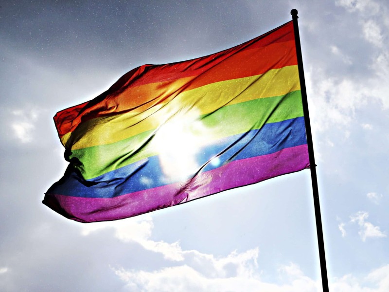 A photo of the pride flag against a pale blue sky, covering the sun.