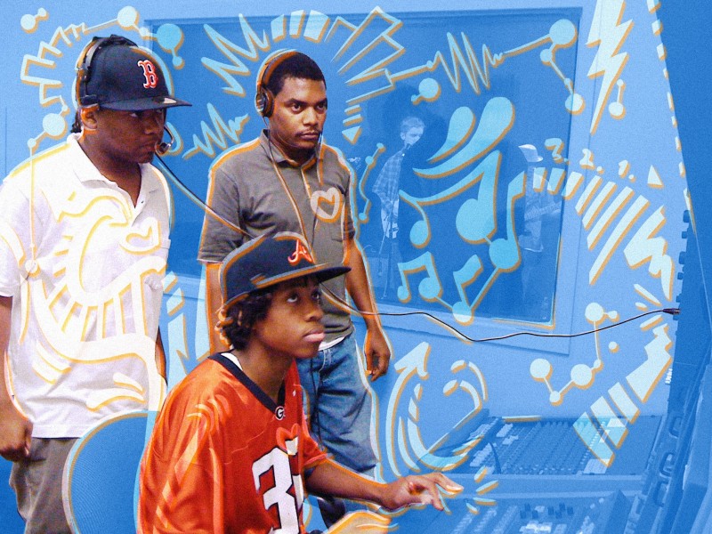 In a TV booth, Antoine Haywood, a Black man, and a Black youth in a white polo, are standing and listening through headphones to a segment another Black youth in an orange jersey, seated, is putting together. A blue and orange overlay is layered over the photo.