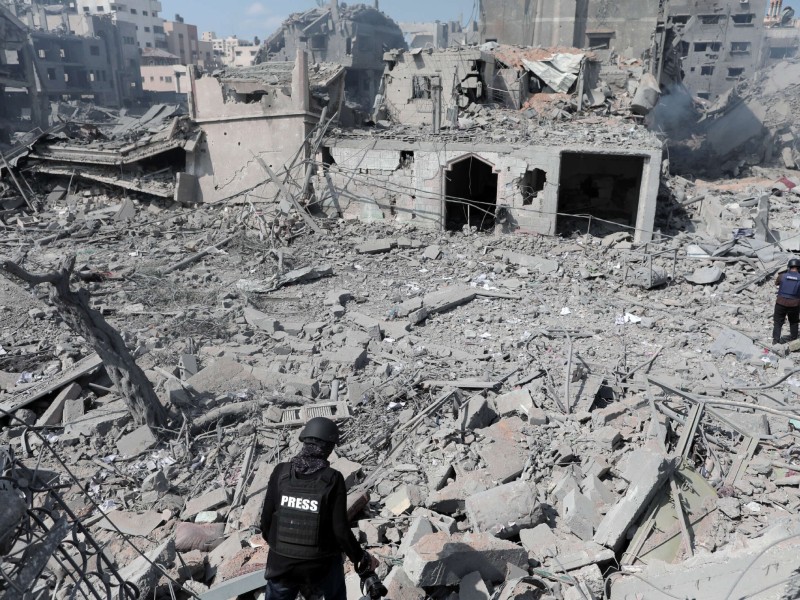 Two members of the Palestinian press traverse and evaluate the rubble of several buildings left behind by Israeli airstrikes.