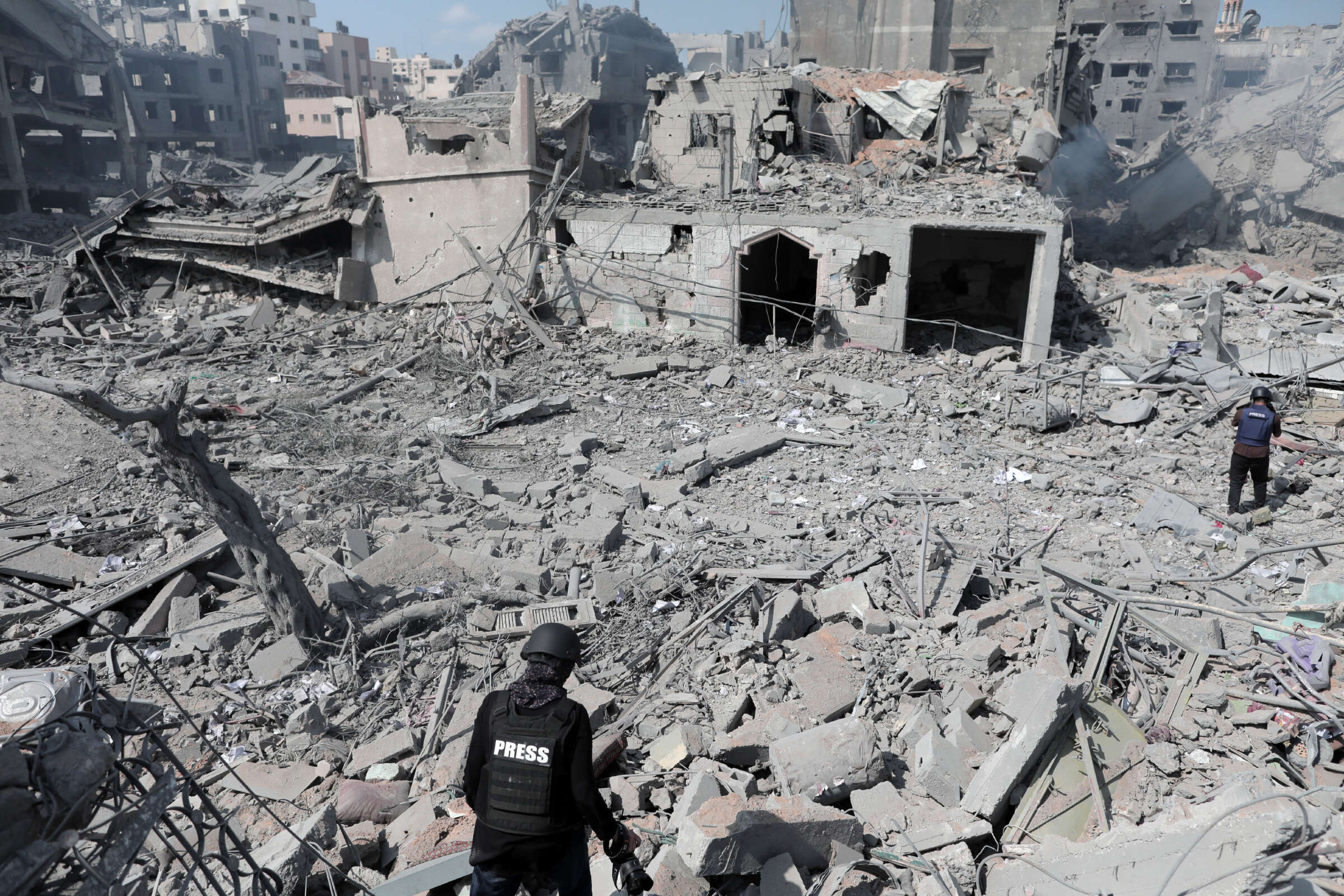 Two members of the Palestinian press traverse and evaluate the rubble of several buildings left behind by Israeli airstrikes.