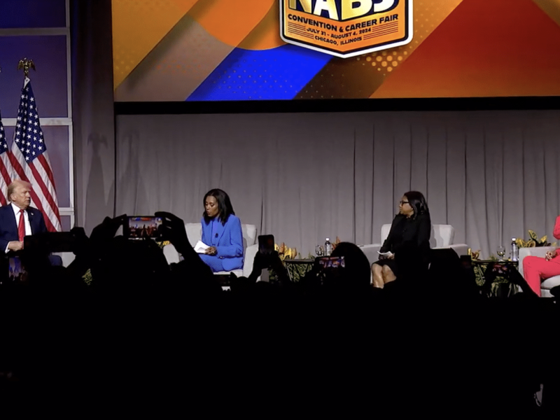 Former president Donald Trump sits in front of three American flags on stage with three Black women: ABC News host Rachel Scott, Semafor political reporter Kadia Goba, and Fox News host Harris Faulkner, from left to right.