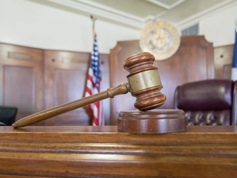 A gavel perched in front of an empty courtroom bench.