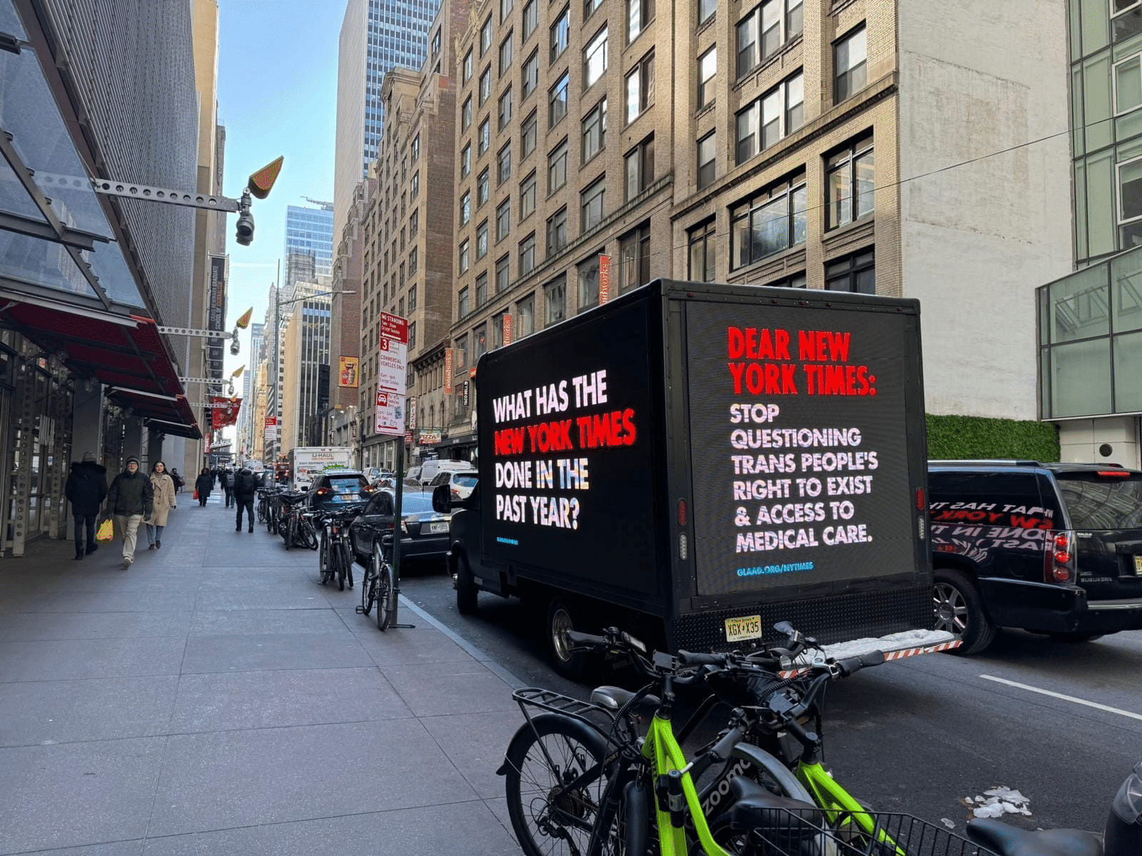 A truck with a GLAAD digital billboard sits next to the New York Times building. The side of the truck reads: What has the New York Times done in the past year? The back of the truck reads Dear New York Times: Stop questioning trans people's right to exist & access to medical care. A link to glaad.org/nytimes is underneath the text.