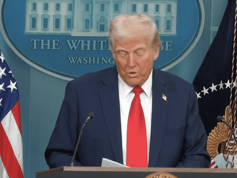 Donald Trump looks down at a podium to read notes in the White House press conference room.