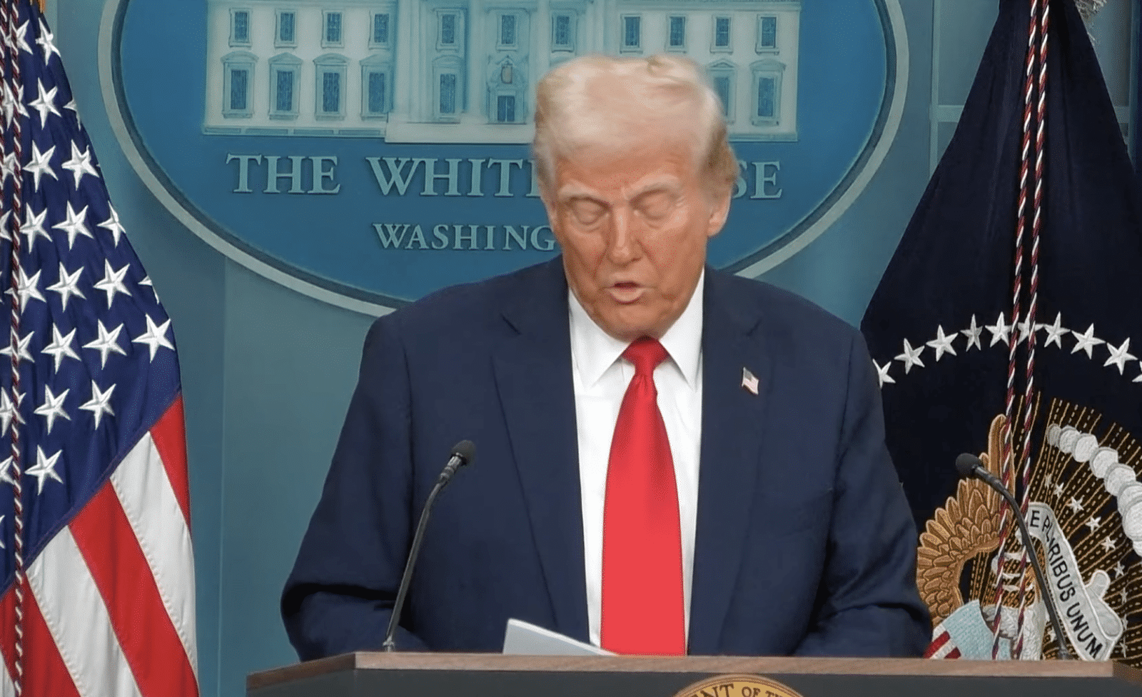 President Donald Trump looking down at notes on a podium in the White House press conference room.