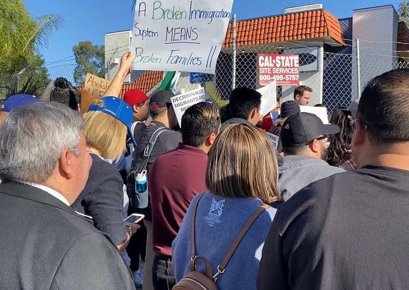 A crowd of people gathers to protest outside a new ICE detention facility in Arleta. One person holds a poster saying "A broken immigration system means broken families."