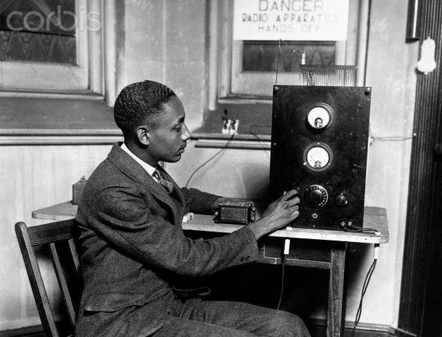 A black and white photo of a young Black man, Rufus P. Turner, sitting and fiddling with a radio at a desk.