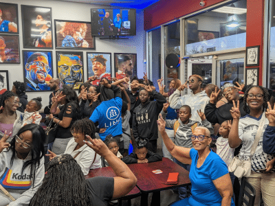 Black mothers and their children pack a restaurant, smiling and posing for the camera.