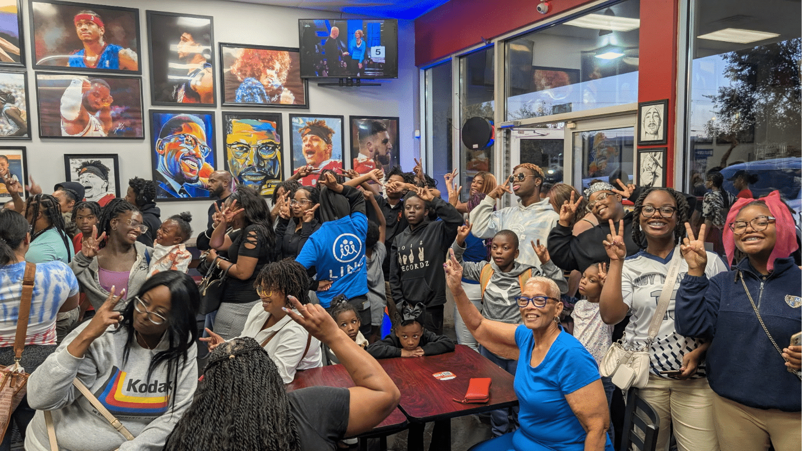 Black mothers and their children pack a restaurant, smiling and posing for the camera.