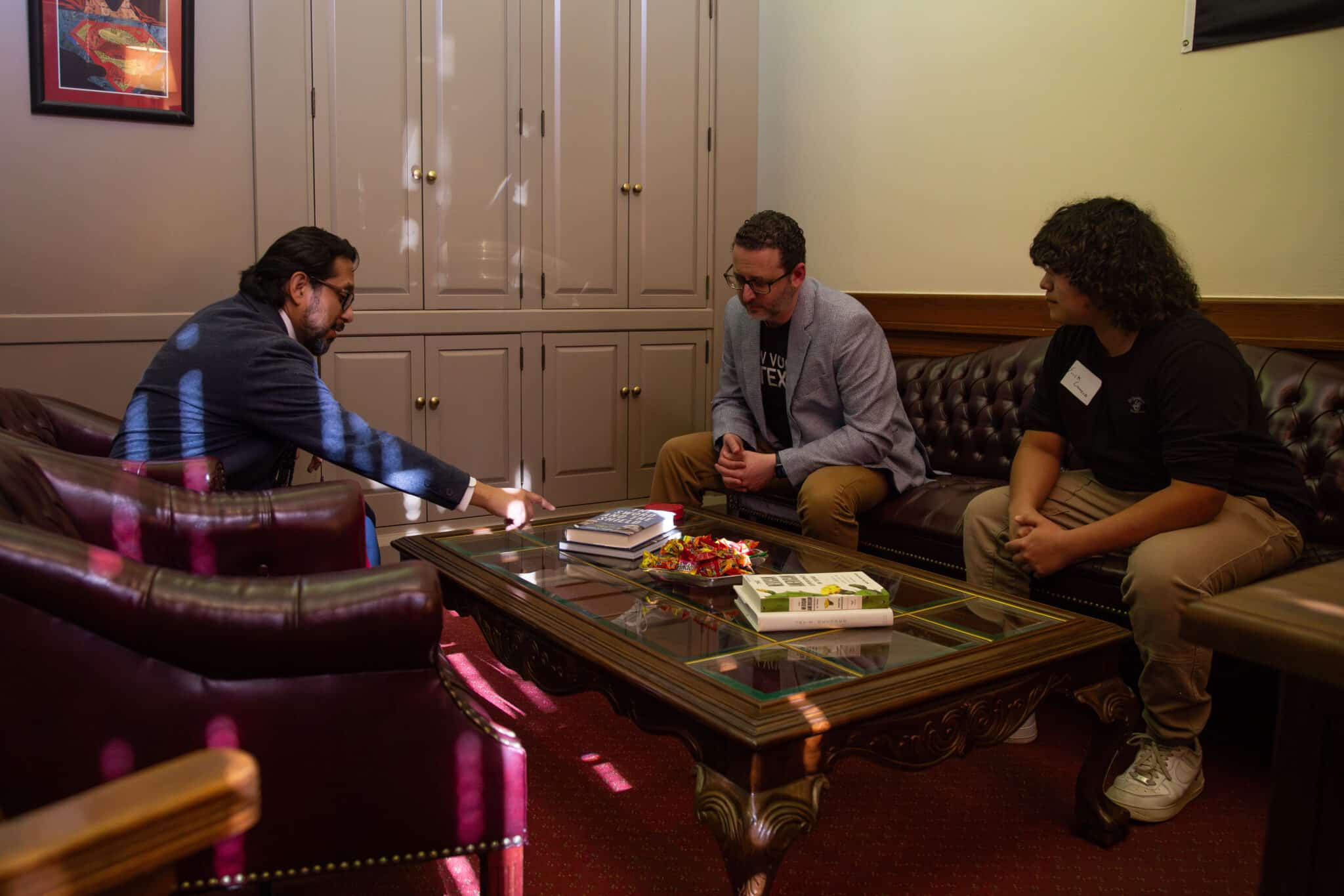 Two members of the New Voices Texas movement, an advisor and a high school advocate, sit across a Texas representative. The three are engaged in conversation.