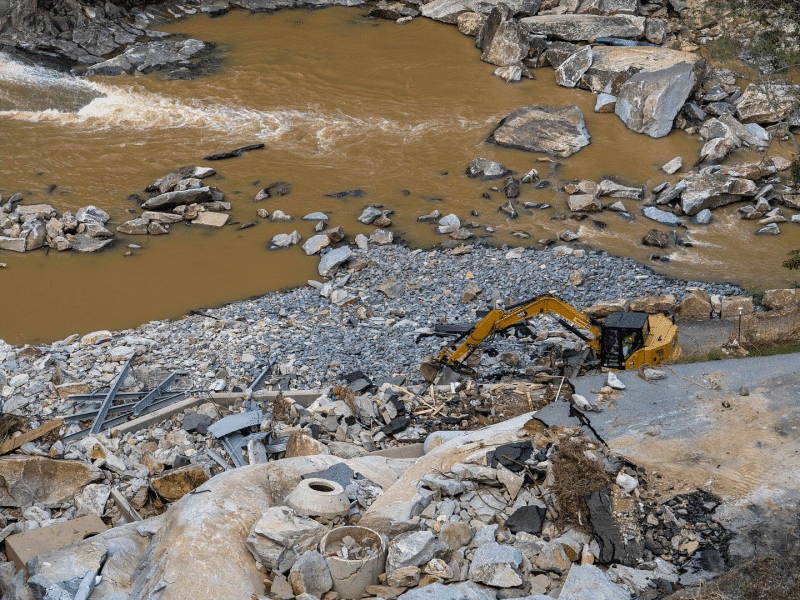 Next to a flooded area, a yellow crane truck picks up debris caused by Hurricane Helene.