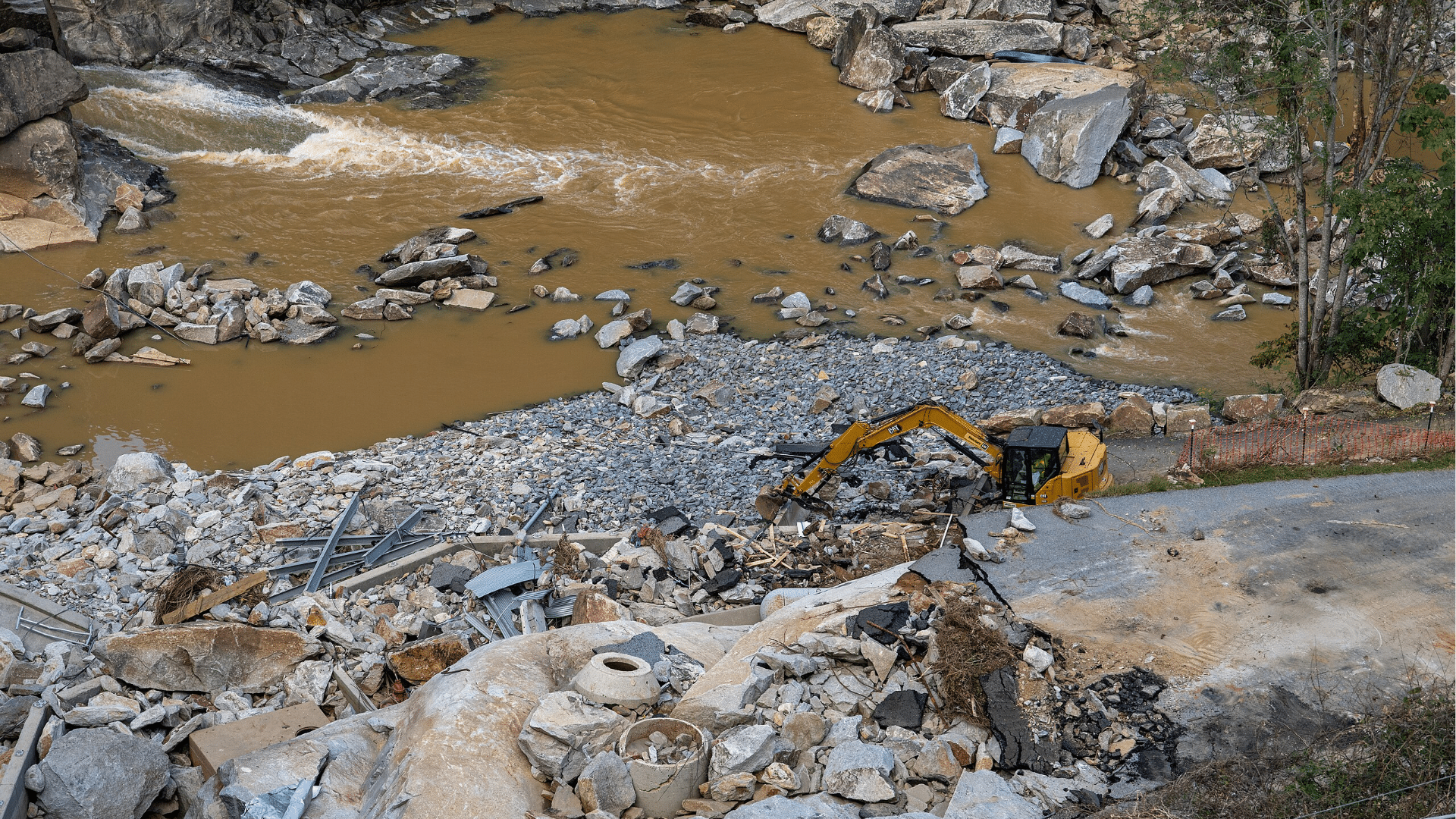 Next to a flooded area, a yellow crane truck picks up debris caused by Hurricane Helene.
