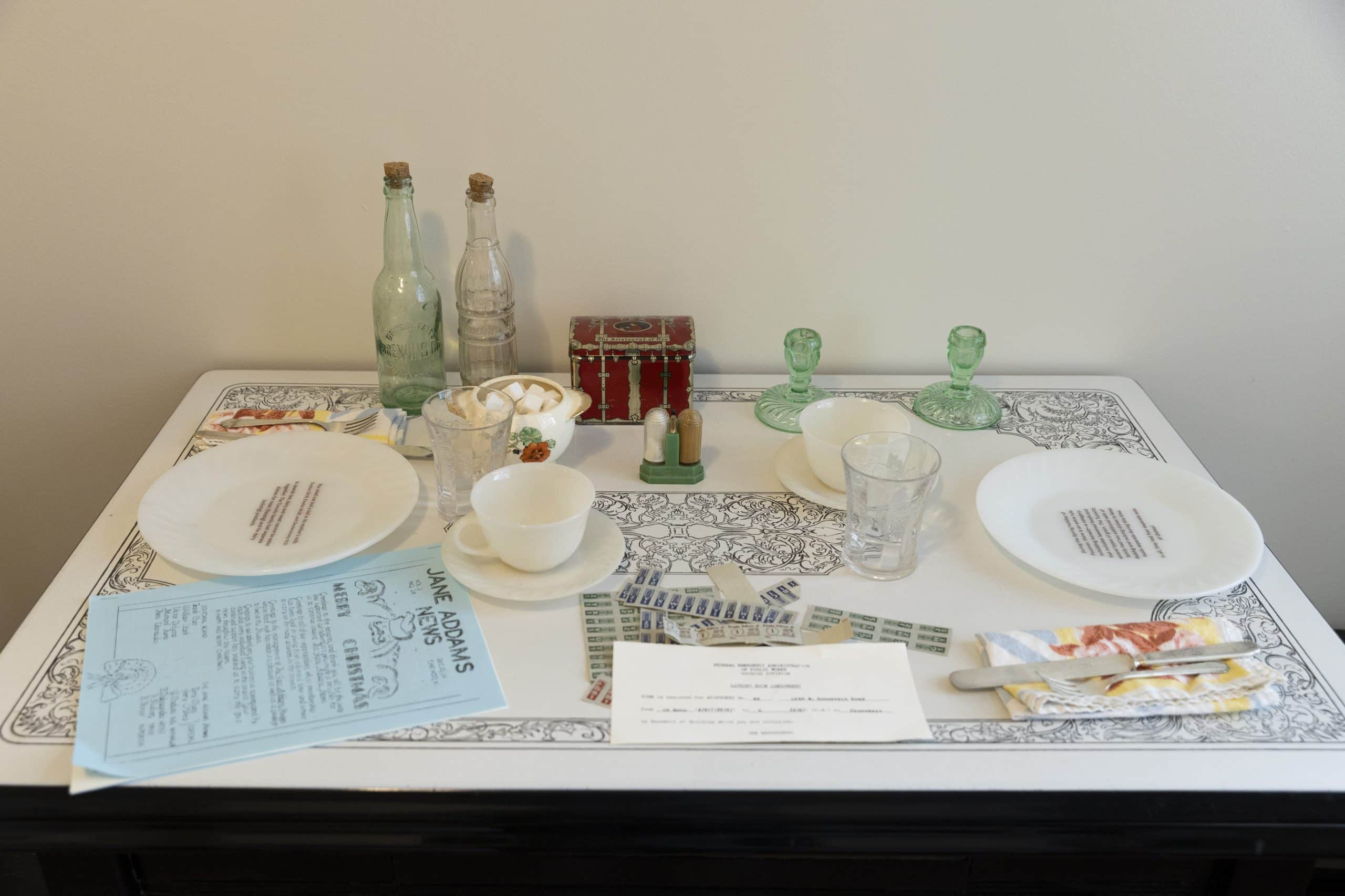 A place setting reproduction with a reproduced copy of the Jane Addams News, the building newsletter for the Jane Addams apartments.