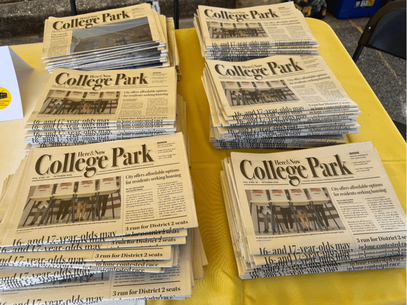 A table piled with College Park Here & Now papers.
