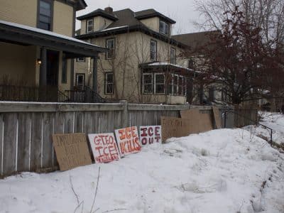 Anti-ICE messages on five cardboard signs line the fence of a house, reading: Immigrants Built America, GTFO ICE! Ur killers. ICE Kills. ICE Out. Fuck this shit.