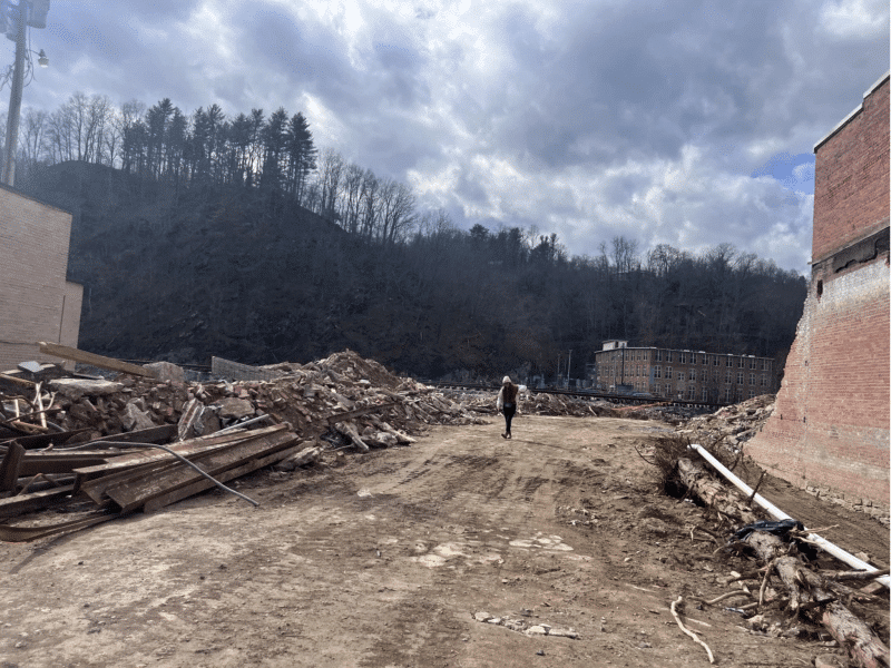 A person walks along a dirt path in downtown Marshall, North Carolina, flanked by debris after Hurricane Helene.