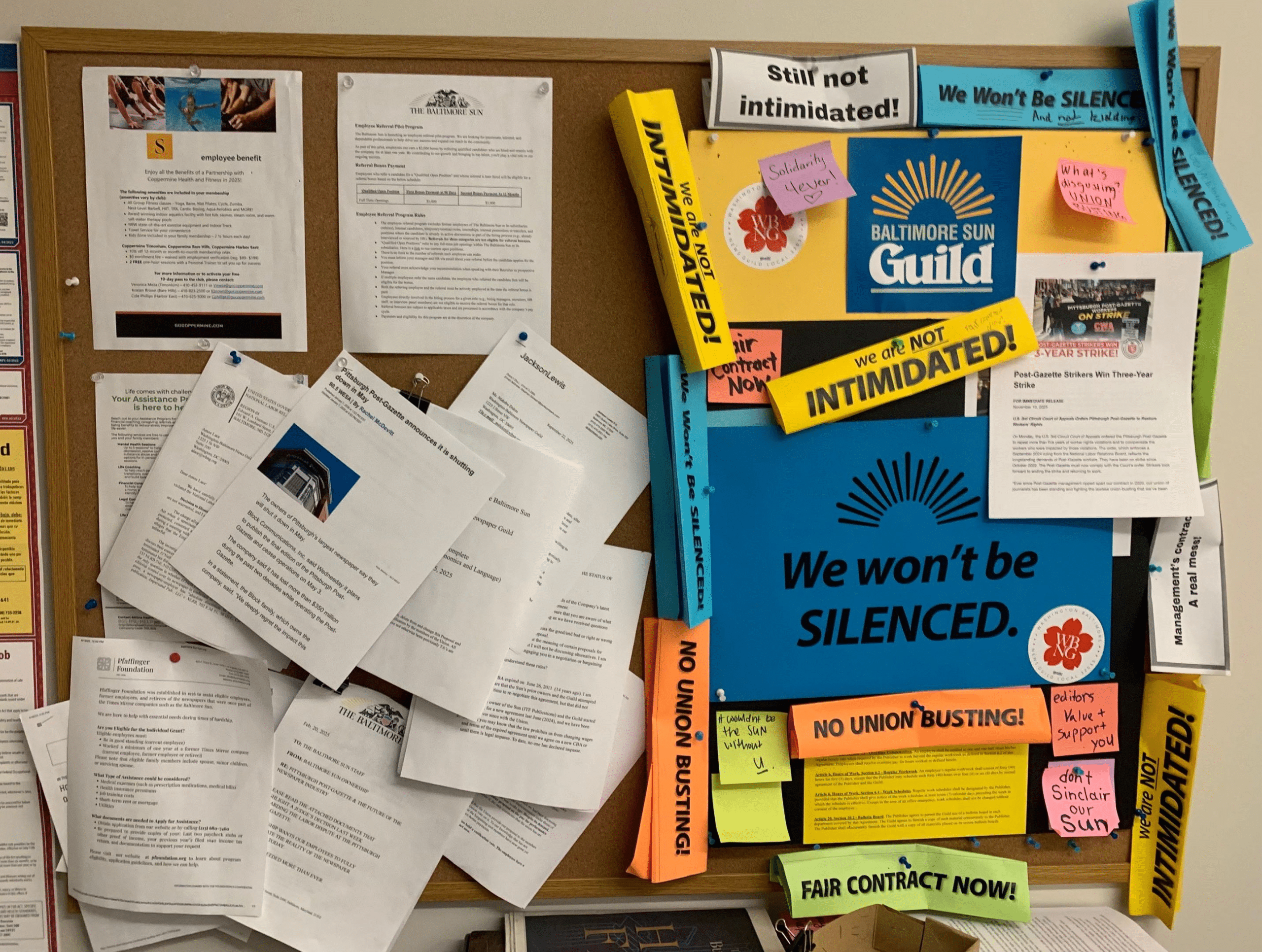 The left side of a billboard is filled with news stories about the Pittsburgh Post-Gazette closing after its reporters' three-year strike. The right side of the billboard is filled with union posters that say things like "Still not intimidated!" "We are not intimidated!" "We won't be silenced." 