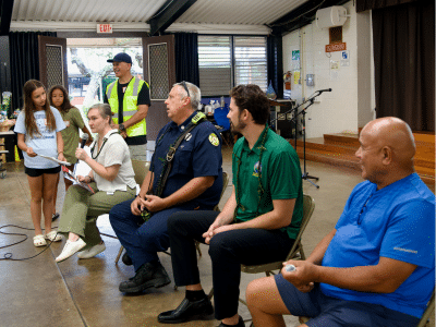Papakōlea homestead residents sit together talking to two fire officials n a multipurpose building setting to discuss wildfire preparedness.