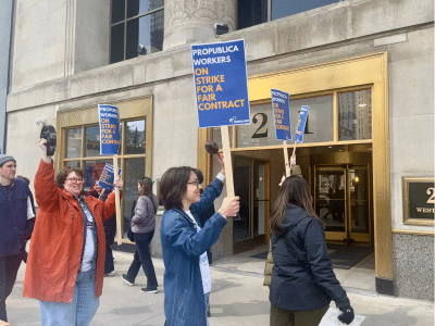 Several workers in a circle picketing the Chicago office of ProPublica hold up signs that say "ProPublica workers on strike for a fair contract."