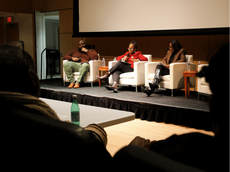 Three Black journalists, from left to right, Tramon Lucas, Dr. Kaye Whitehead, and Errin Haines sit facing an audience in a town hall session.