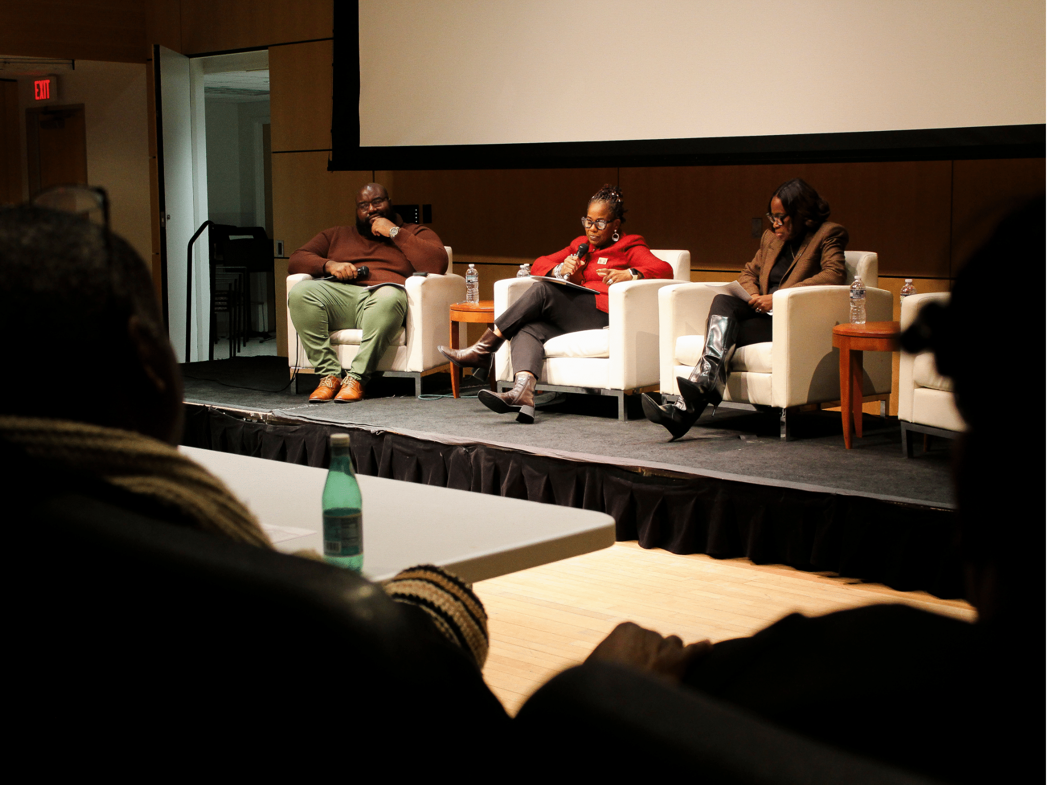 Three Black journalists, one man (Tramon Lucas) and two women (Dr. Kaye Whitehead and Errin Haines), sit facing an audience in a town hall session.
