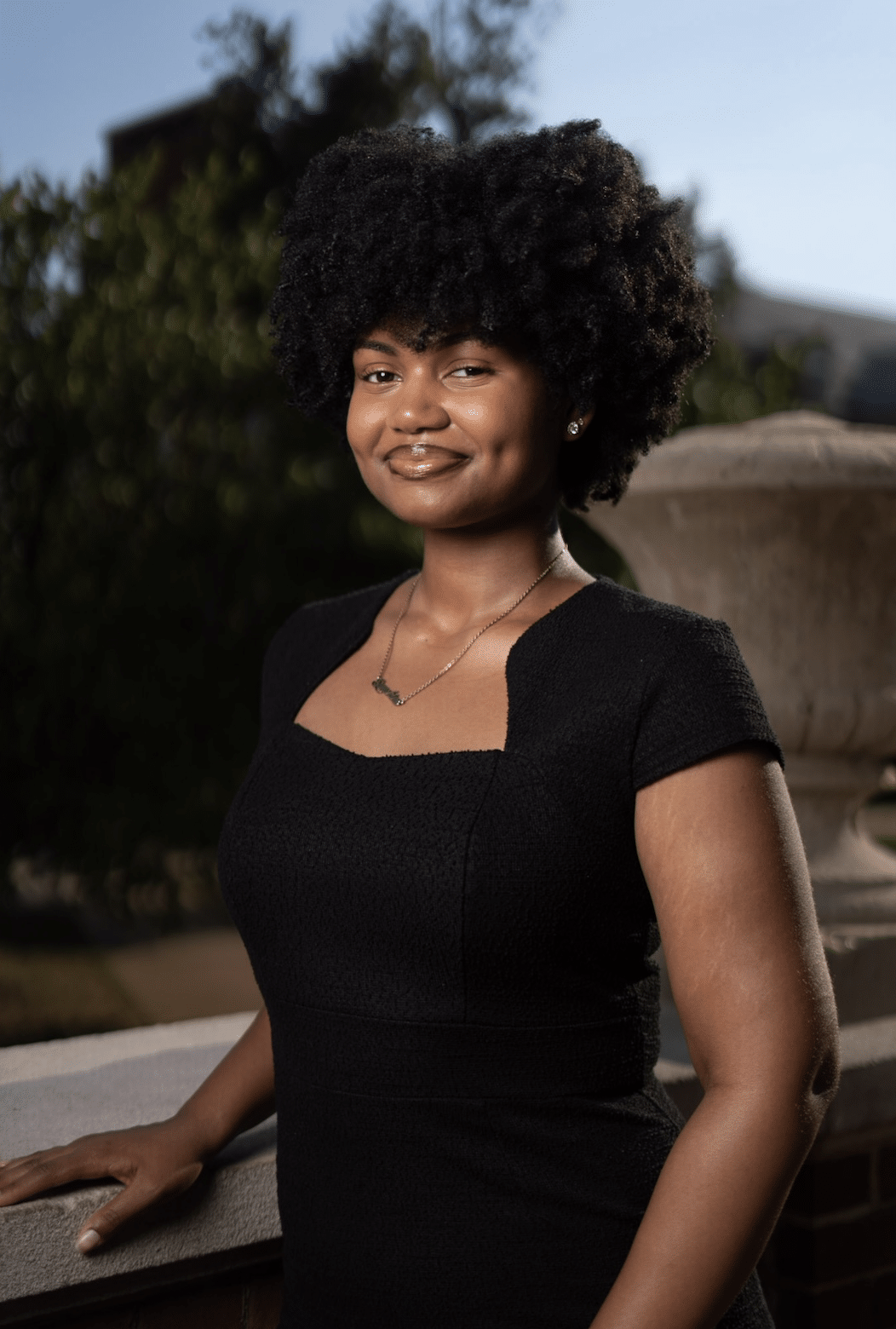 Headshot of Tatiana Allen, a young Black woman with natural hair worn in a twist out above her shoulders. She wears a cap-sleeve black top and smiles at the camera.