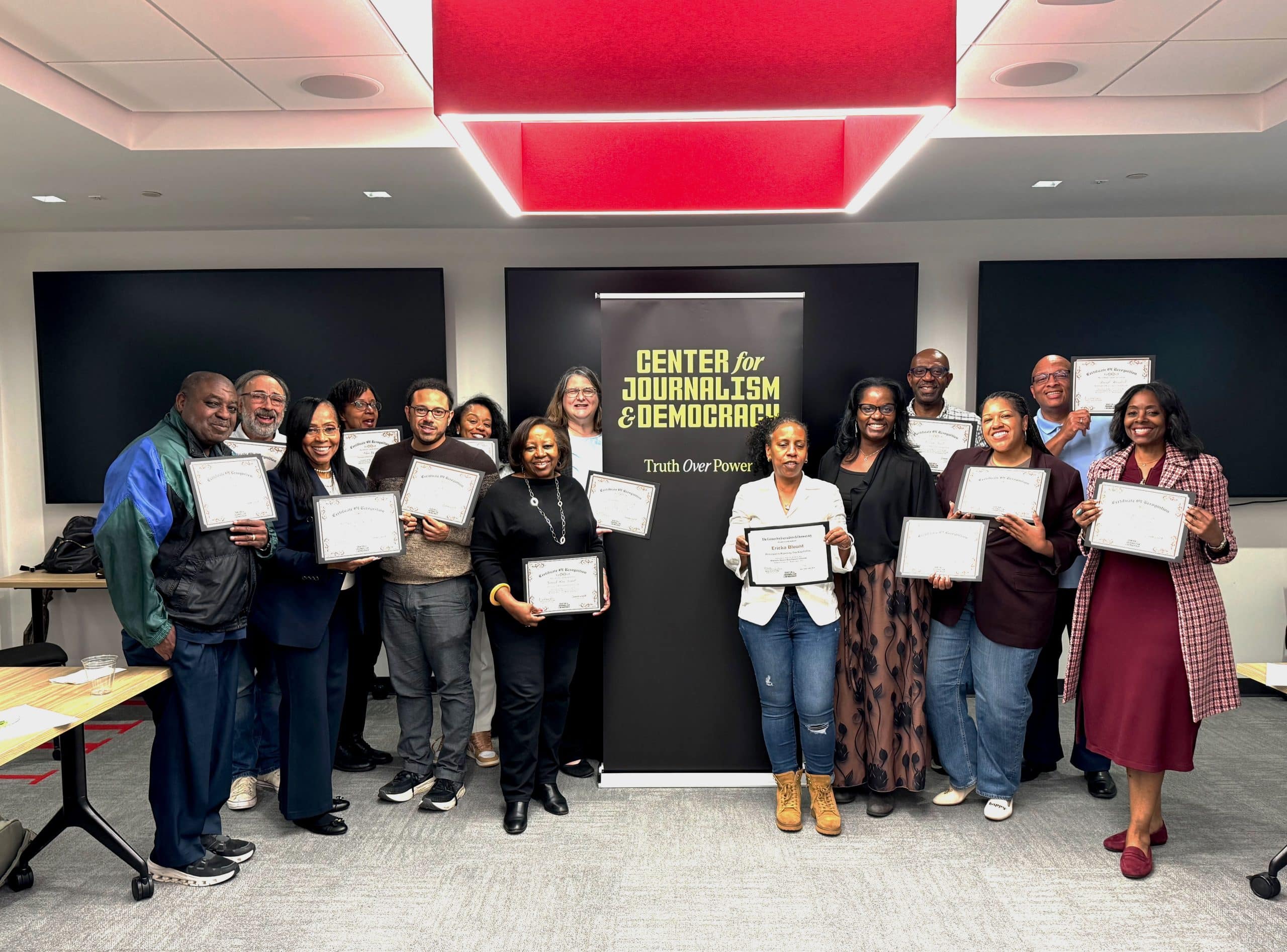 A collection of professors, most of them Black, of mixed genders, standing next to a banner that reads Center for Journalism & Democracy: Truth Over Power. 