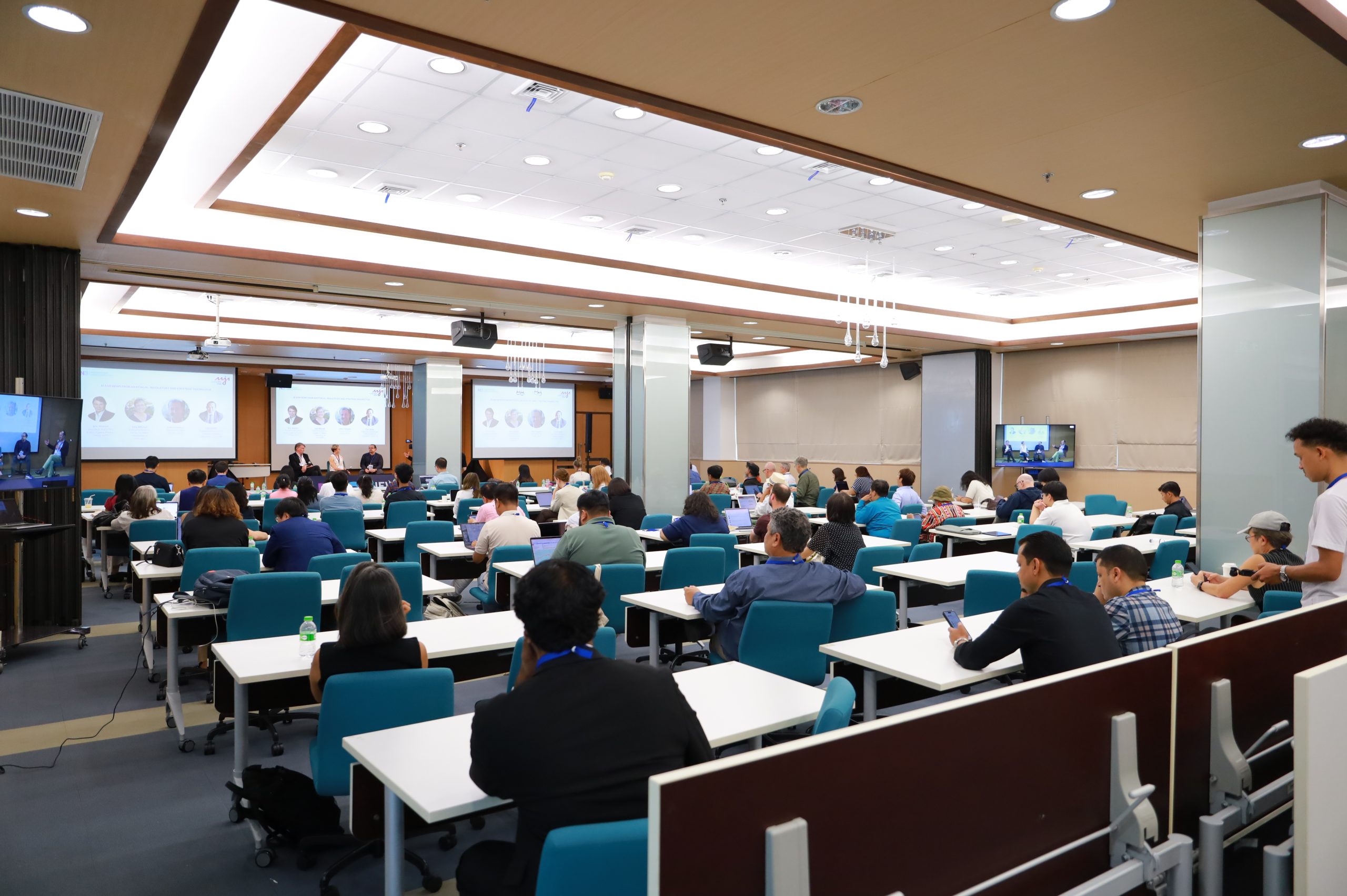 About 20-30 journalists fill a classroom watching four speakers at the front. 