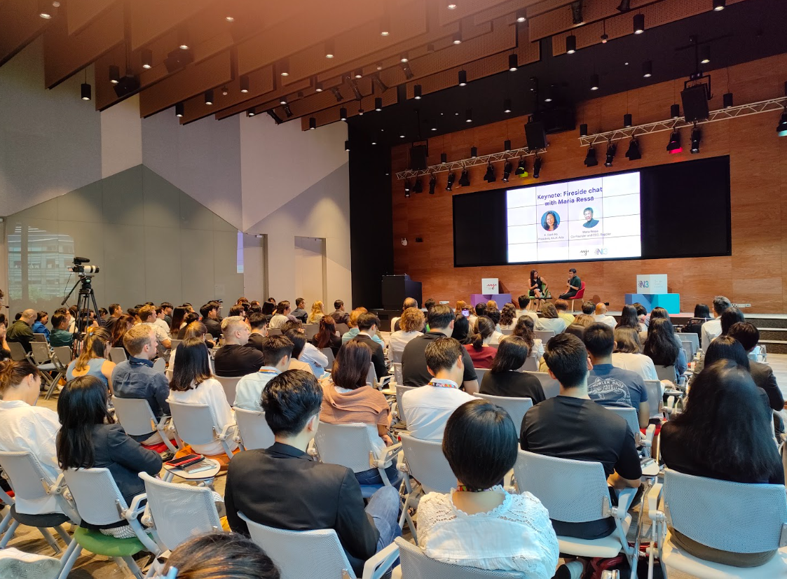 A full crowd of dozens of journalists fills a medium-size room watching Filipino journalist Maria Ressa, who is wearing a button-up and has short, close-cropped hair, talk with then-AAJA Asia president, K. Oanh Ha, who is wearing a dress and has black hair past her shoulders.